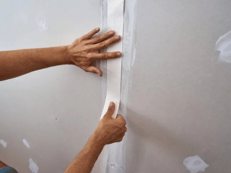 hand installing tape and bed on drywall